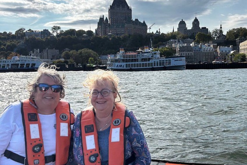 Two people on a boat with life jackets, a river, and a cityscape with historic buildings in the background. 2