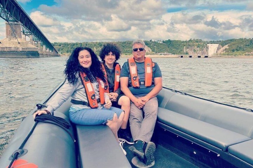 Three people on a boat with life jackets, a bridge in the background, and water. 5
