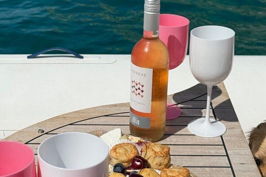 A bottle of wine, a glass, and pastries on a wooden table by a body of water. 3