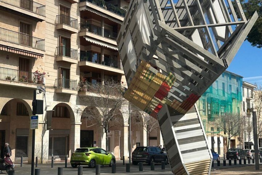 A modern building with a tilted structure, parked cars, and a green car in the foreground. 1