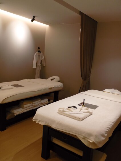 A spa room with two beds, towels, a robe, and a massage table. 2