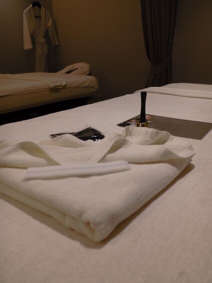 A neatly folded white towel on a bed with a black hairbrush and a small black item on it. 1