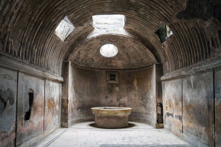 An arched room with a central stone basin, walls with carvings, and a small window. 2