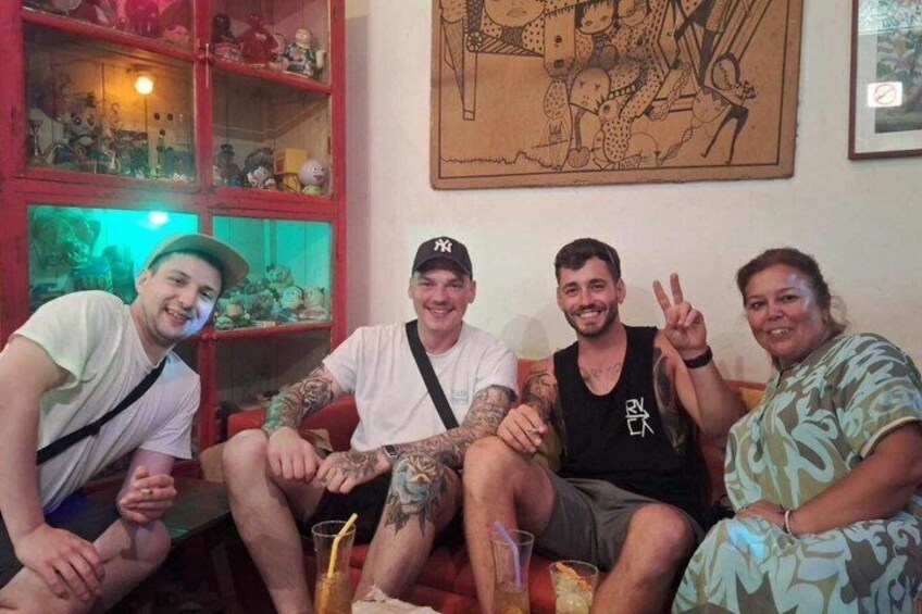 Four people sitting on a couch with a red cabinet and a framed picture in the background. 5