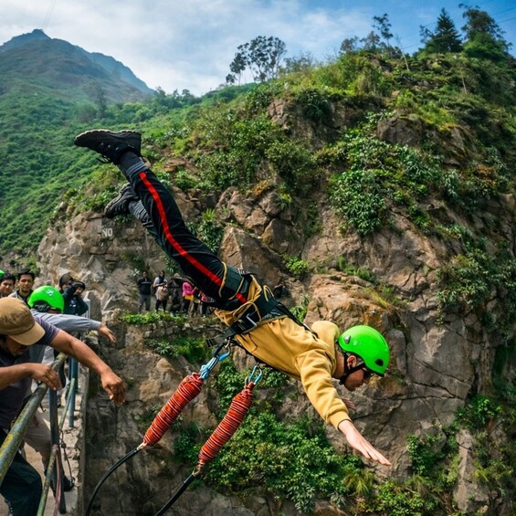 A person bungee jumping with a safety harness and helmet, with a rocky cliff and greenery in the background. 1