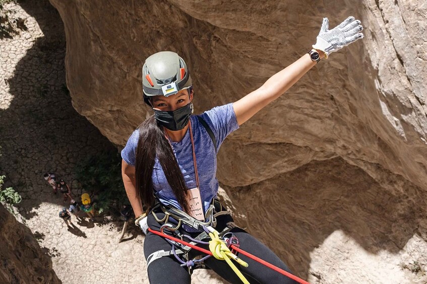 A person rappelling down a canyon with a helmet, harness, and gloves. 2