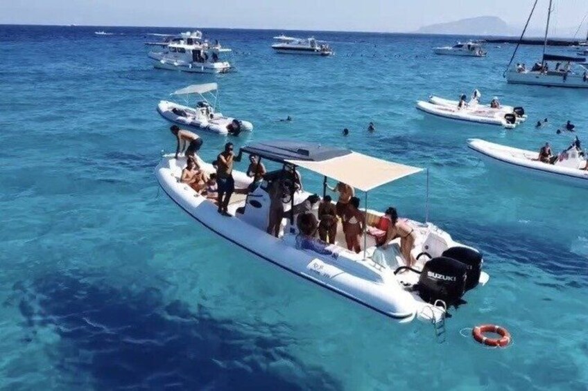 A group of people on a small white boat with a Suzuki engine, surrounded by calm blue waters and other boats. 1