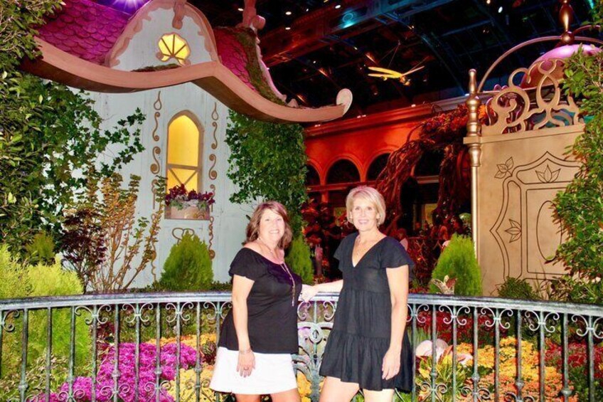 Two people standing in front of a decorative garden with a whimsical house structure and a wrought iron fence. 2