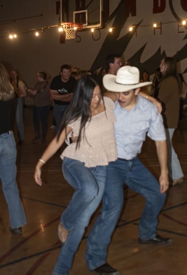 A group of people dancing in a gymnasium with a basketball hoop in the background. 3
