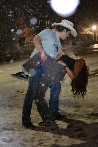 A person in a cowboy hat lifting another person in a snowy outdoor setting. 1