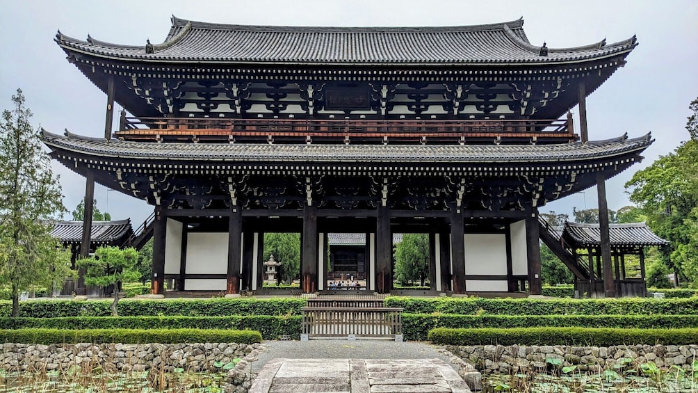 A traditional multi-tiered pavilion with ornate wooden carvings, surrounded by neatly trimmed hedges and a stone pathway leading to the entrance. 4