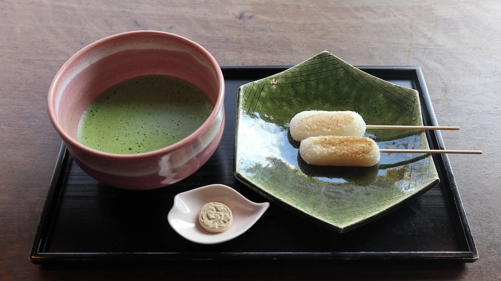 A traditional Japanese tea set with a green tea bowl, a ceramic plate with mochi on skewers, and a small dish with a sweet treat. 5