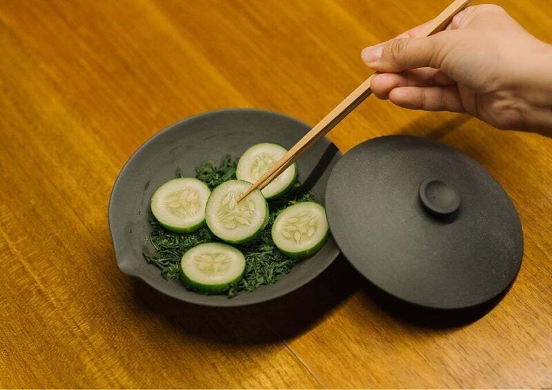 A hand using chopsticks to pick up sliced cucumbers from a bowl. 5