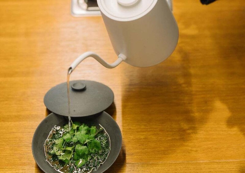 A teapot pouring water onto a plate with green leaves. 4