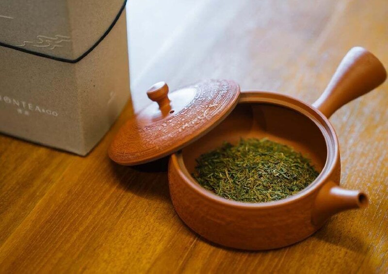 A clay teapot with a lid and a box labeled 'MonteAgogo' on a wooden surface. 3