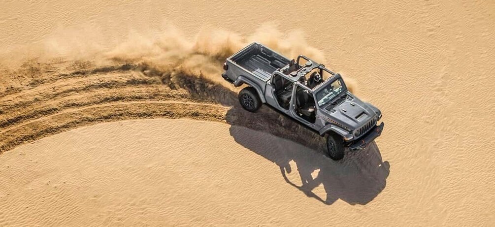 A vehicle driving through a sandy desert, creating a dust trail. 3