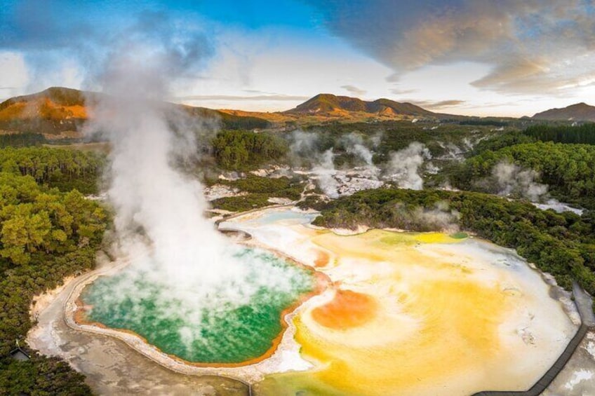 A geothermal area with steam vents, green and yellow hot springs, and a forested landscape. 1
