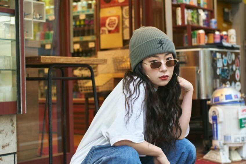 A person sitting on a chair outside a store with shelves stocked with various items. 5