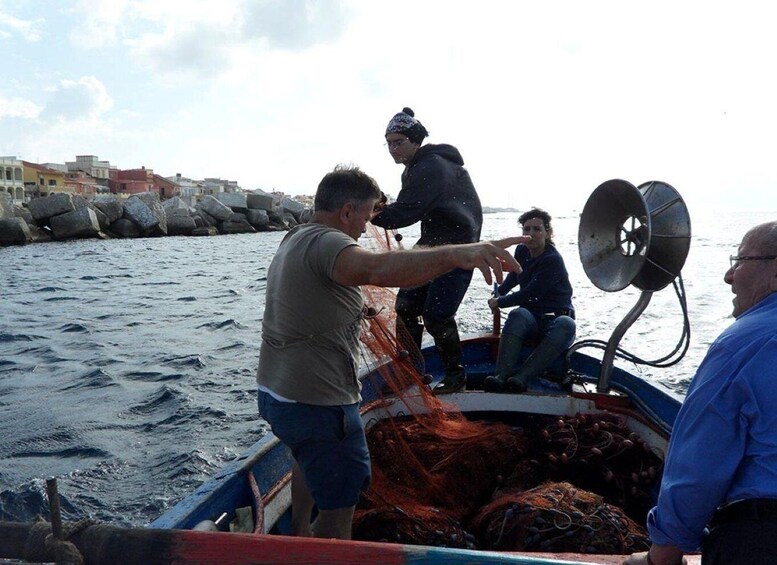 A group of people on a boat with fishing nets, rocky shore, and buildings in the background. 3