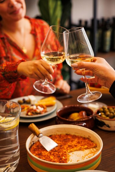 A person holding a wine glass, a bowl of food, and a water glass on a table. 4