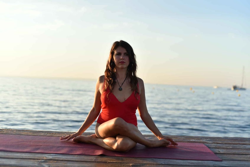 A person sitting on a yoga mat by the water. 1