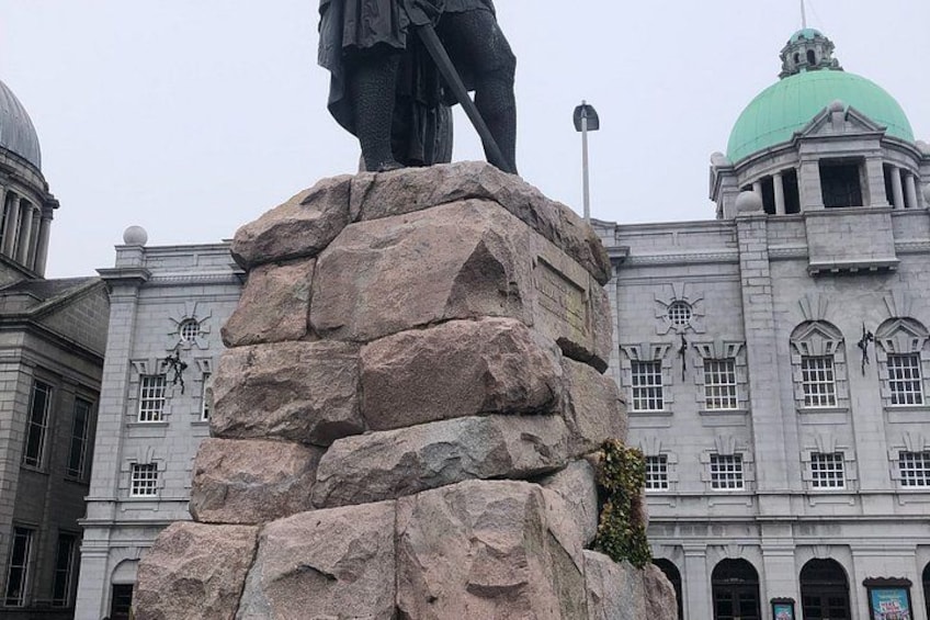 A statue on a rock pedestal in front of a building with a green dome and arched windows. 2