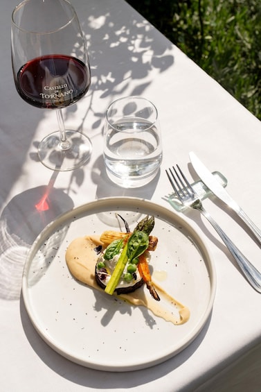 A white plate with a gourmet dish, a glass of red wine, and cutlery on a table with a white tablecloth. 3