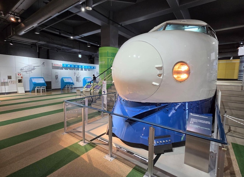 A space shuttle on display with a blue and white exterior, surrounded by informational panels and a green cylindrical structure. 1