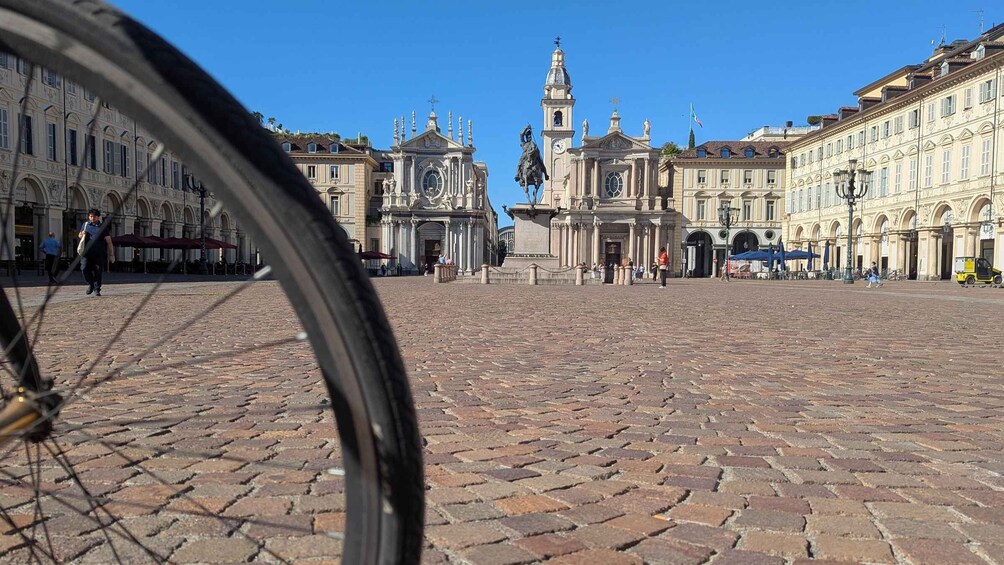 A cobblestone square with historic buildings, a clock tower, and a statue. 1