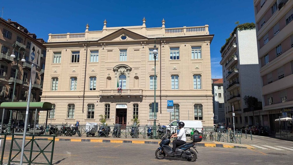 A historic building with a central entrance, multiple windows, and a flag. 2