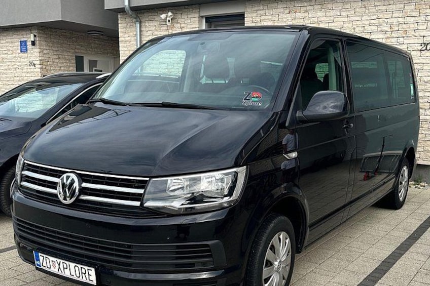 A black Volkswagen van parked in front of a building with a brick facade. 2