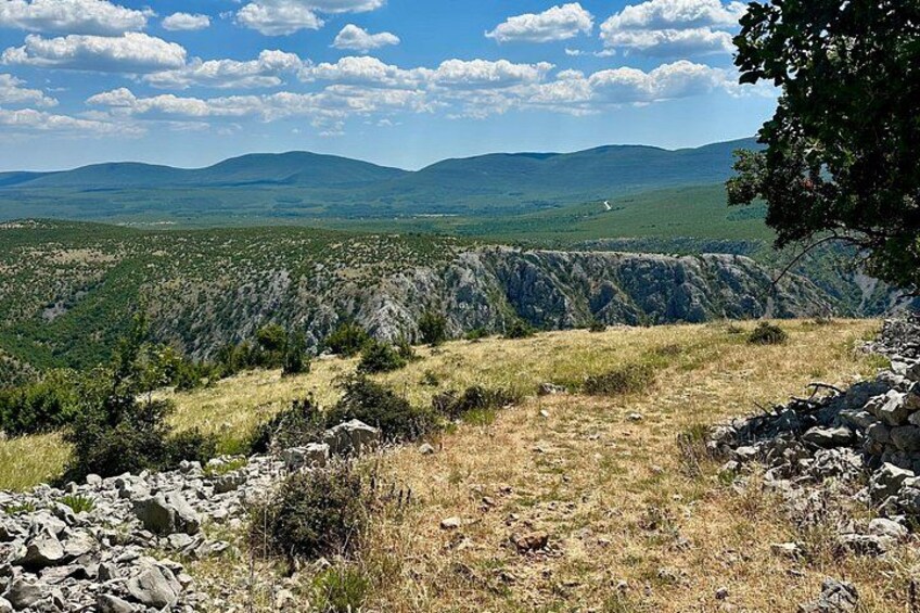 A mountainous landscape with rocky terrain, sparse vegetation, and distant hills under a partly cloudy sky. 5