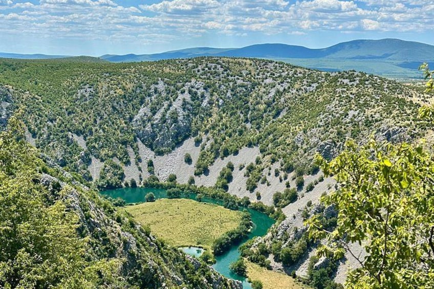A mountainous landscape with a river, green valley, and distant hills. 1