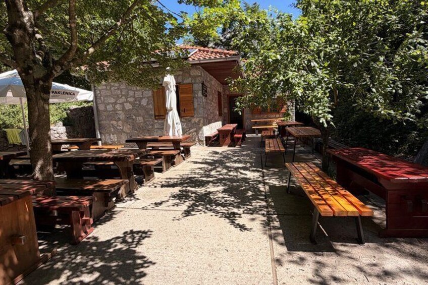 A rustic outdoor seating area with wooden tables and benches, surrounded by trees and a stone building. 5