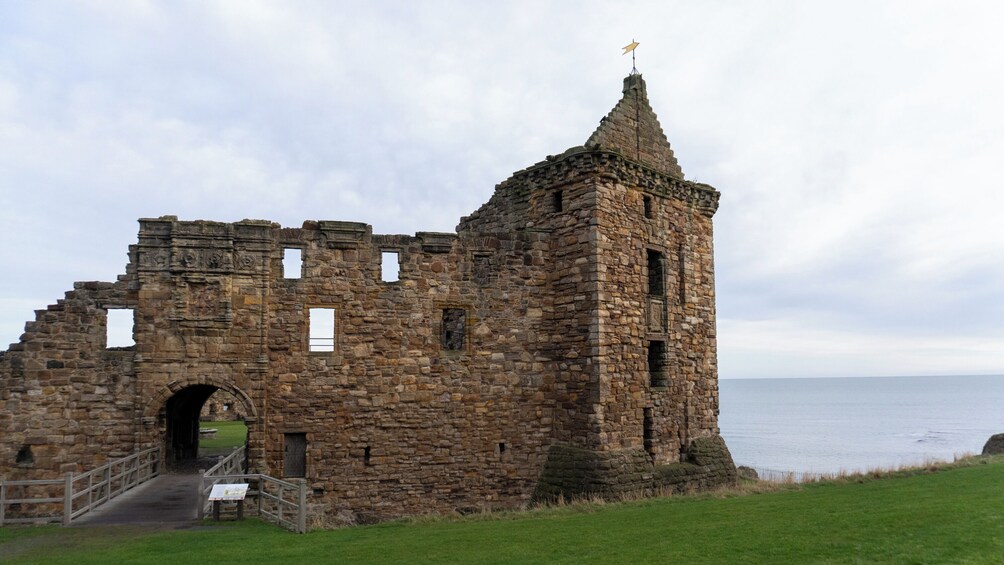 A stone ruin with a tower, a grassy foreground, and a body of water in the background. 5