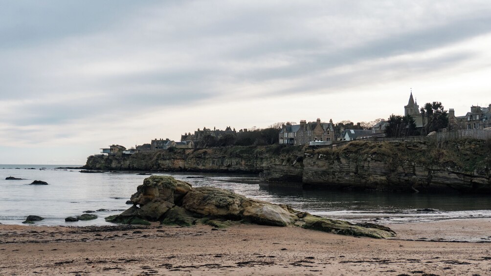 A coastal town with buildings on a cliff, a sandy beach, and rocky outcrops. 2