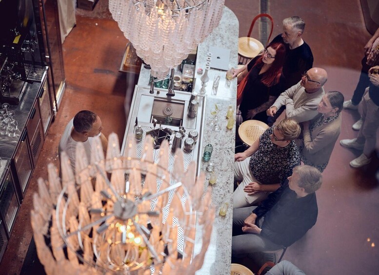 A group of people gathered around a bar area with a chandelier and bar tools. 3