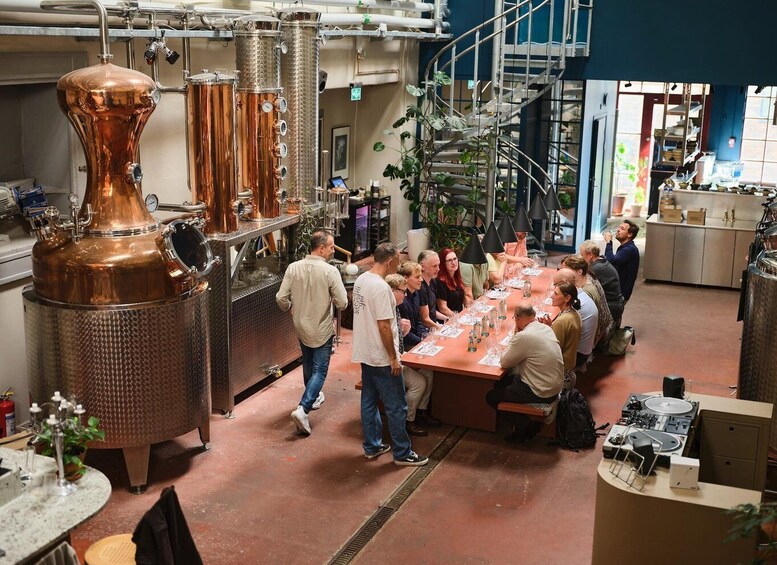A group of people gathered around a long table in a room with industrial copper distillation equipment. 4