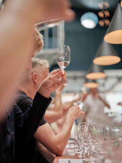 A person holding a wine glass at a dining table with other empty glasses and a person in the background. 5