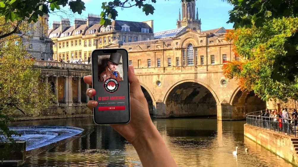 A hand holding a smartphone with a 'GO QUEST ADVENTURES' app interface, a historic building, a bridge, and a river with a swan. 1