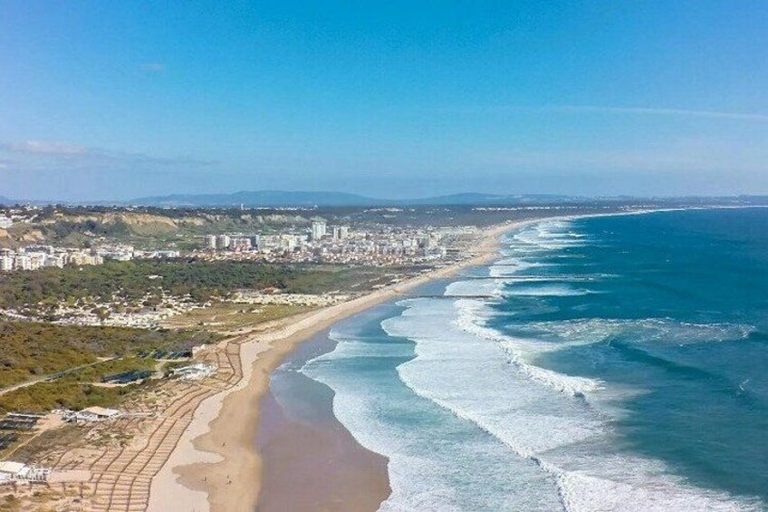 A coastal cityscape with a long beach, clear blue ocean, and urban buildings. 4