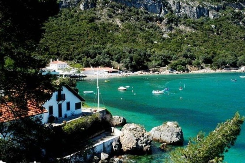 A coastal village with a white house, clear turquoise waters, boats, and a rocky shoreline. 1