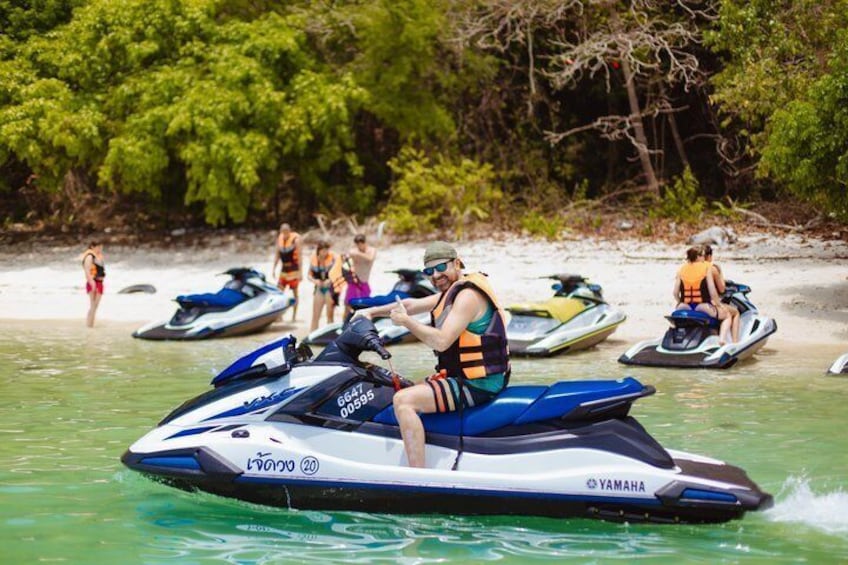 A person riding a jet ski on a beach with other jet skis and people in the background. 1