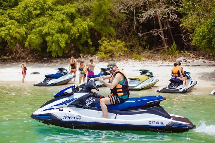 A person riding a jet ski on a beach with other jet skis and people in the background. 1