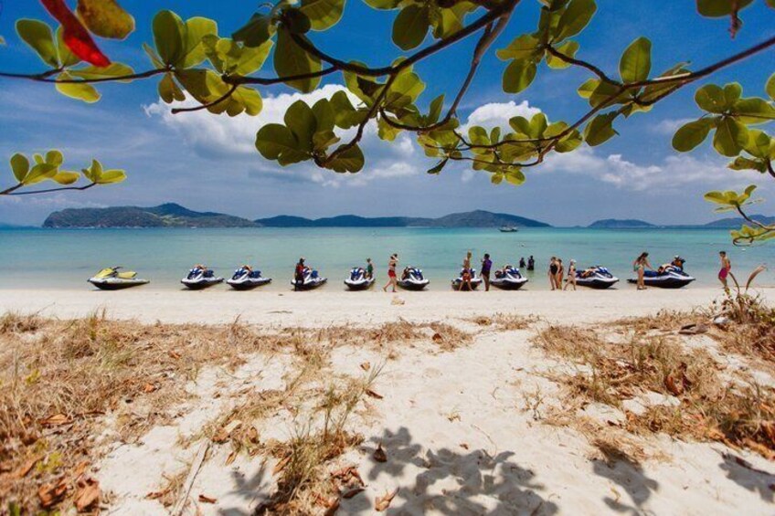 A beach with several jet skis lined up on the sand, a clear sky, and distant mountains. 5