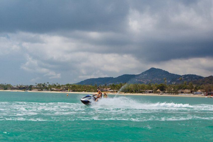 A person jet-skiing on turquoise water with a beach and mountains in the background. 4