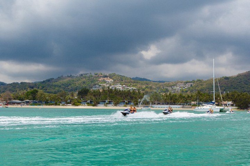 A coastal scene with a boat speeding across turquoise waters, a sailboat, and a hilly landscape with buildings in the background. 3