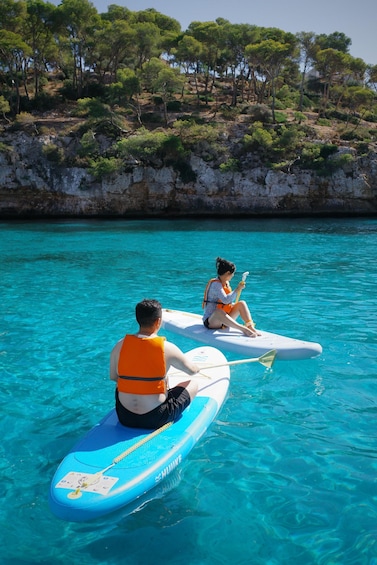 Two people on paddleboards in a clear blue body of water with a rocky shoreline and trees in the background. 5