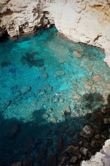 A clear turquoise sea with rocky formations and a person swimming. 3