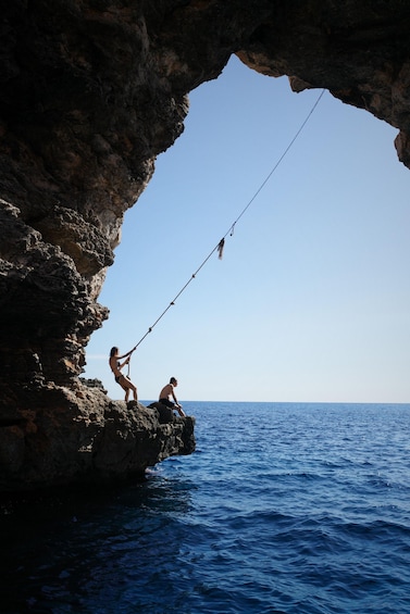 Two people fishing from a rocky cave entrance overlooking the sea. 2